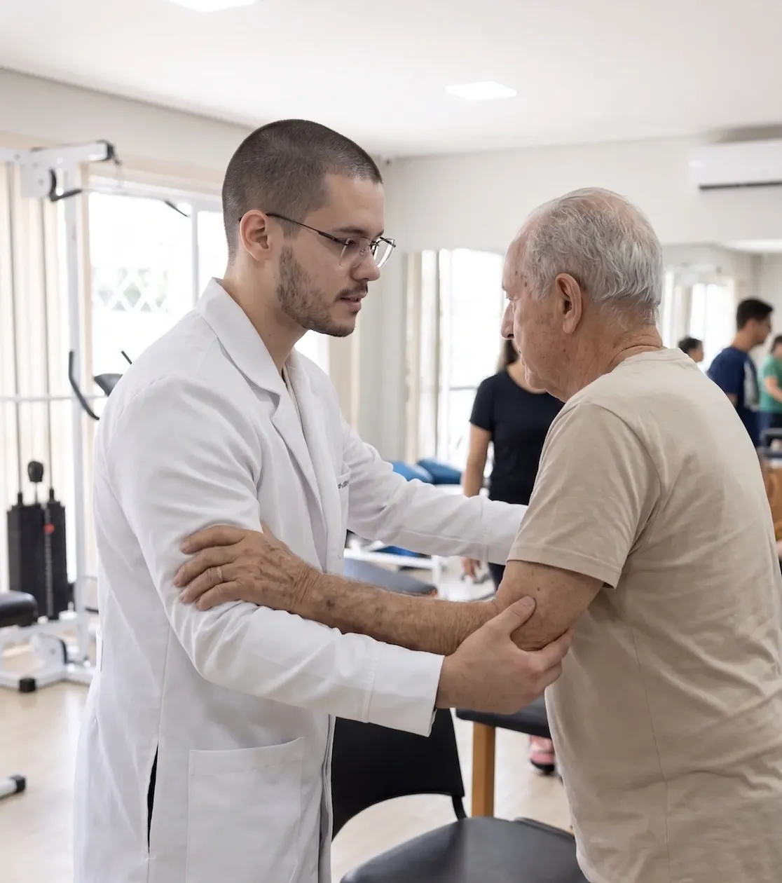 Dr. Yuri Noronha avaliando e auxiliando paciente idoso com dor no ombro em atendimento domiciliar